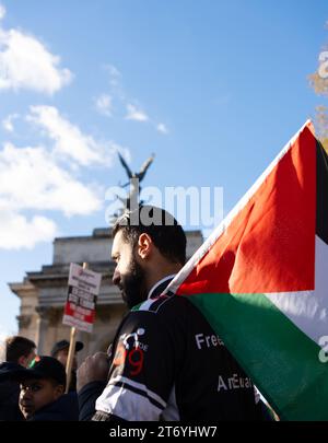 L'homme tient le drapeau palestinien devant l'arche Wellington de Londres pendant la marche de la paix. Le soleil d'automne attrape son visage et ses cheveux avec une lumière dure. Banque D'Images