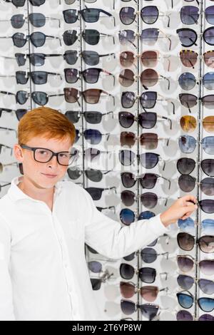 Garçon choisissant des lunettes regardant caméra optica Banque D'Images