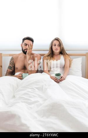 Jeune couple avec tasse café assis lit Banque D'Images