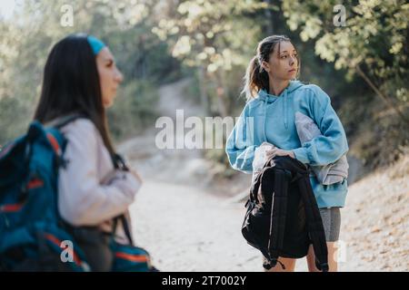 De jeunes amis marchent à travers la forêt d'automne, embrassant le voyage d'aventure. Engagés dans des conversations amusantes, ils profitent de l'air frais et font de l'exercice à l'extérieur. Banque D'Images