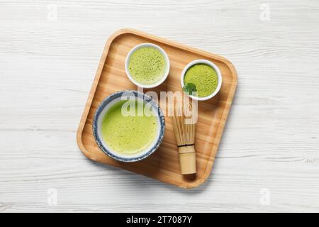 Thé matcha frais, fouet en bambou et poudre verte sur table en bois blanc, vue de dessus Banque D'Images