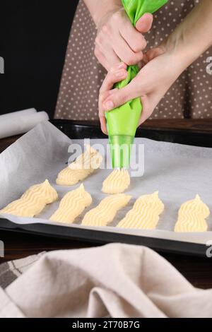 Faire des eclairs. Femme pressant la pâte crue du sac à pâtisserie sur la plaque de cuisson à la table, gros plan Banque D'Images