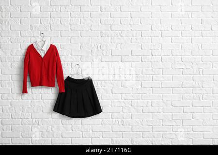 Uniforme scolaire élégant accroché sur le mur de briques claires dans la chambre Banque D'Images