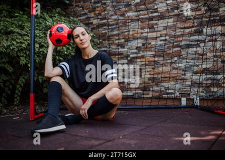 Belle joueur de football féminin debout par but de football avec balle dans sa main. La femme joue au football pour se détendre. Concept de santé mentale et Banque D'Images