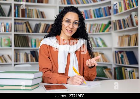 Jeune enseignante hindoue conduit des leçons en ligne dans la salle de classe assise à la table, faisant des gestes avec les mains et écrivant dans le cahier, vue de la caméra, employé de bureau ayant un appel vidéo de travail regardant la caméra. Banque D'Images