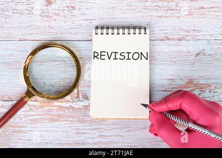 RÉVISION écrivant sur un cahier allongé sur de vieux tableaux à côté d'une loupe et une main dans un gant médical rouge avec un crayon Banque D'Images