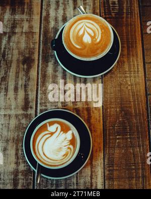 Deux tasses blanches en céramique avec des motifs complexes contenant des boissons chaudes à base de café à la vapeur sur une table en bois Banque D'Images