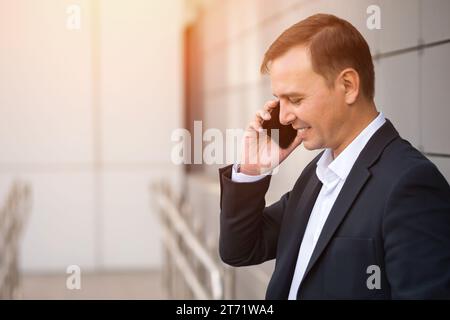 Homme d'affaires souriant adulte en costume parle concerné au téléphone Banque D'Images