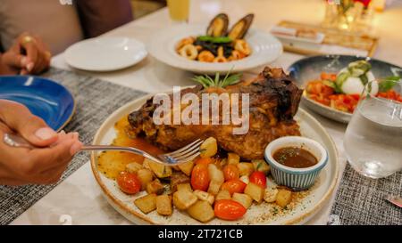 Dîner dans un restaurant italien en Thaïlande, porc cuit lentement, épaule de porc rôtie entière avec une riche marinade chaude épicée sur une table avec du Chili, de l'ail et du romarin. vue d'en haut, gros plan Banque D'Images