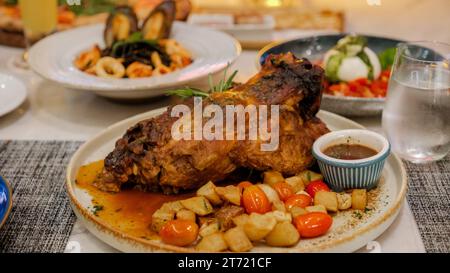 Dîner dans un restaurant italien en Thaïlande, porc cuit lentement, épaule de porc rôtie entière avec une riche marinade chaude épicée sur une table avec du Chili, de l'ail et du romarin. vue d'en haut, gros plan Banque D'Images