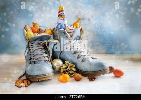 Bottes de randonnée remplies de bonbons, fruits et décoration de Noël, tradition sur Sinterklaas ou en Allemagne Nikolaus Tag au 6 décembre, boke bleu clair Banque D'Images