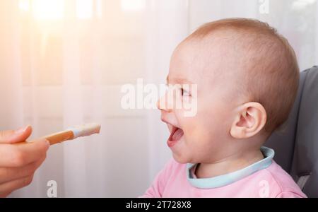 Mère nourrit le bébé caucasien porridge de sarrasin, bébé avec la bouche ouverte, gros plan. Copier l'espace pour le texte Banque D'Images