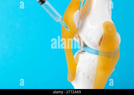 Injection intra-articulaire de médicaments anti-inflammatoires dans une maquette d'articulation du genou sur fond bleu. Le concept de blocage médicamenteux pour soulager la douleur Banque D'Images
