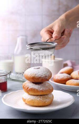 Femme saupoudrant le sucre en poudre sur de délicieux beignets Hanukkah sur la table gris clair, gros plan Banque D'Images