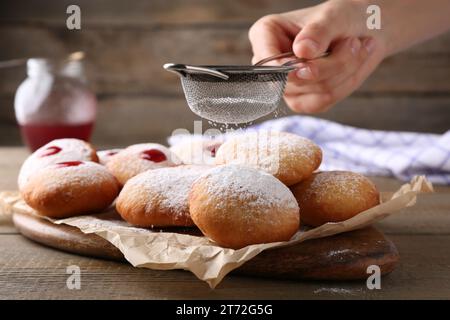 Femme saupoudrant le sucre en poudre sur de délicieux beignets Hanukkah sur la table en bois, gros plan Banque D'Images