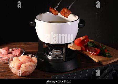 Tremper des morceaux de viande frite dans de l'huile dans un pot à fondue à la table en bois Banque D'Images