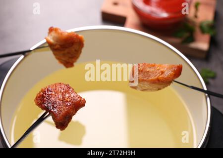 Huile dans une casserole à fondue et des fourchettes avec des morceaux de viande frits sur la table, gros plan Banque D'Images