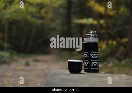 Thermos noir et couvercle de tasse sur banc en bois à l'extérieur, espace pour le texte Banque D'Images