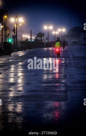 Un cycliste portant des vêtements de haute visibilité chevauchant le long de la promenade sous la pluie sur un Worthing Beach matin de novembre, Worthing, Royaume-Uni le 13 novembre 2023. Photo de Julie Edwards. Banque D'Images