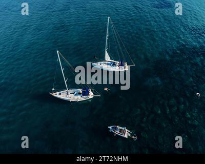 Yachts à voile ancrés dans la mer bleue, vue de dessus. Yacht à voile sur fond sombre, vue aérienne. Banque D'Images