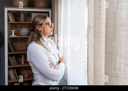 Jeune femme psychologue confiante regardant par la fenêtre du bureau à domicile. Une travailleuse en santé mentale faisant une pause après une conversation psychologique Banque D'Images