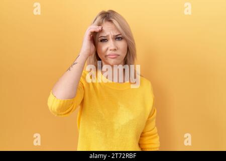 Jeune femme caucasienne portant un pull jaune inquiète et stressée par un problème de main sur le front, nerveuse et anxieuse pour la crise Banque D'Images