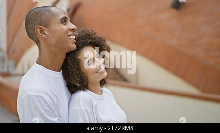 Beau couple, étreint et souriant, regarde avec confiance le ciel sur une rue de la ville bourdonnante. pleins d’amour et de joie, ils partagent ce moment heureux Banque D'Images