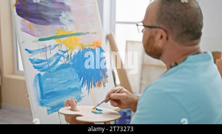 Bel homme caucasien d'âge moyen, un artiste profondément concentré alors qu'il dessine passionnément un portrait dans son atelier d'art intérieur Banque D'Images