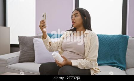 Inquiète jeune femme hispanique attendant bébé consulte le médecin en ligne à partir du canapé à la maison, parlant de graves problèmes de grossesse Banque D'Images