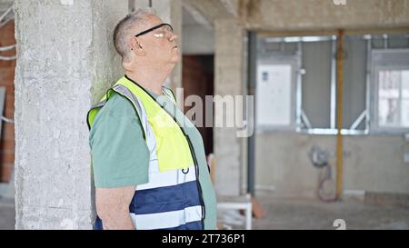 Homme d'âge moyen aux cheveux gris s'appuyant sur le mur fatigué sur le chantier de construction Banque D'Images