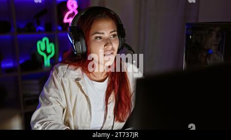 Streamer pour jeune femme rousse, plongé dans une séance de jeu intense, dans un jeu virtuel sérieux, casque allumé, encapsulé dans un éclairage tamisé Banque D'Images