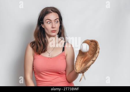 Femme en T-shirt rose attrape balle avec un gant de baseball. Expression faciale surprise. Banque D'Images