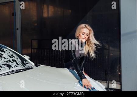 une femme blonde lave une voiture à un lavage de voiture de l'eau propre de voiture dans un tuyau pour une voiture Banque D'Images