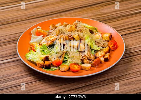 Salade César avec poulet et feuilles de salana sur une assiette orange sur une table en bois Banque D'Images