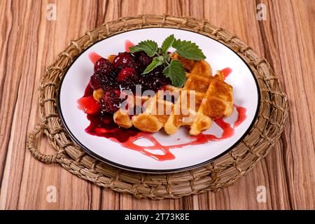 Biscuits gaufrés sucrés, versés avec de la confiture de baies dans une assiette blanche sur un plateau en osier Banque D'Images