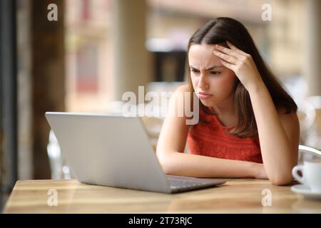 Femme frustrée vérifiant le contenu de l'ordinateur portable dans une terrasse de bar Banque D'Images