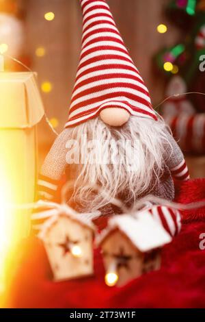 Jouet de Noël gnome avec un chapeau rayé sur sa tête et guirlandes brillantes. Banque D'Images