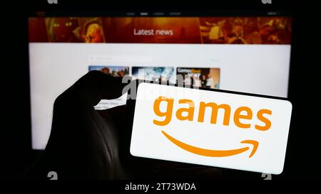 Personne tenant le téléphone mobile avec le logo de la société américaine de jeux vidéo Amazon Games devant la page Web d'affaires. Concentrez-vous sur l'affichage du téléphone. Banque D'Images