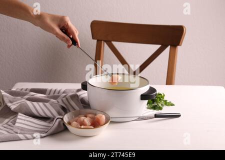 Femme trempant morceau de viande crue dans l'huile dans le pot à fondue à la table en bois blanc, closeup Banque D'Images