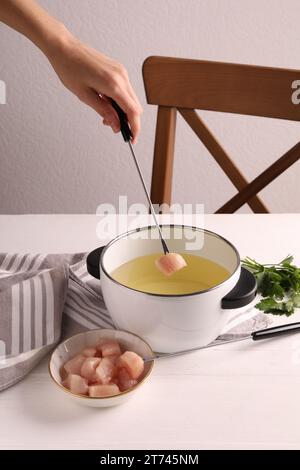 Femme trempant morceau de viande crue dans l'huile dans le pot à fondue à la table en bois blanc, closeup Banque D'Images