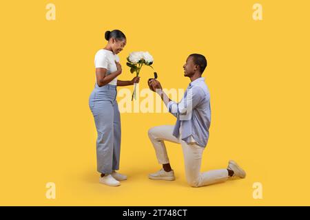 Homme noir proposant avec anneau à la femme tenant des fleurs Banque D'Images
