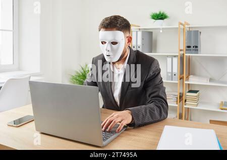 L'homme anonyme dans le masque facial utilise un ordinateur portable pour les affaires en ligne ou l'arnaque sur Internet Banque D'Images