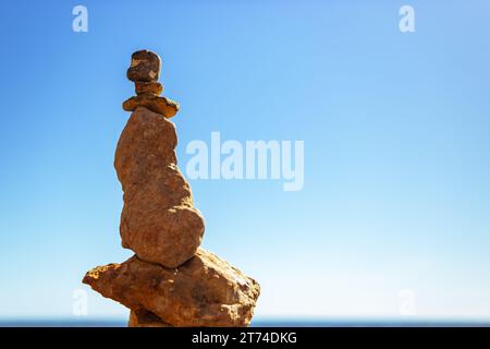 Une pyramide de galets de mer sur une plage de sable ensoleillée contre un ciel bleu. Le concept d'équilibre de vie Banque D'Images