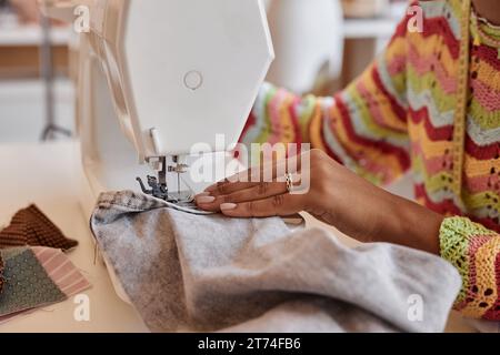 Main de jeune femme afro-américaine coudre des vêtements en denim tout en étant assise devant la machine électrique et en créant de nouveaux articles de mode Banque D'Images