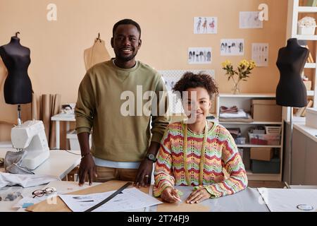 Deux jeunes créateurs de mode afro-américains regardant la caméra avec des sourires tandis que la femme tailleur contournant des patrons de papier à coudre Banque D'Images