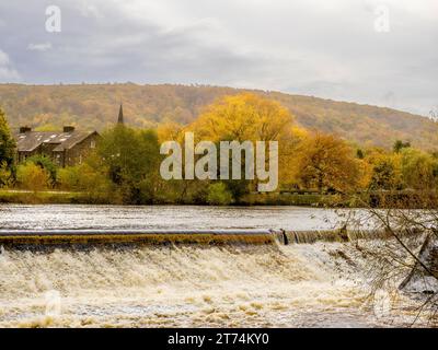 Le déversoir sur la rivière Wharfe à Otley, avec le paysage automnal du parc forestier Otley Chevin s'élevant au loin. Banque D'Images