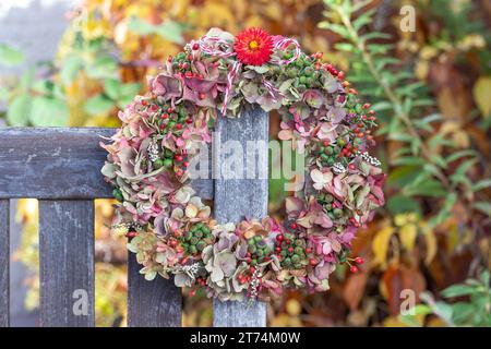 couronne de fleurs d'hortensia, baies de lierre et hanches de rose accrochées sur le banc de jardin Banque D'Images