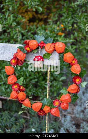 couronne de physalis, fleurs de paille et feuilles de lierre décorées d'une mouche en bois agaric accrochée à une chaise de jardin Banque D'Images