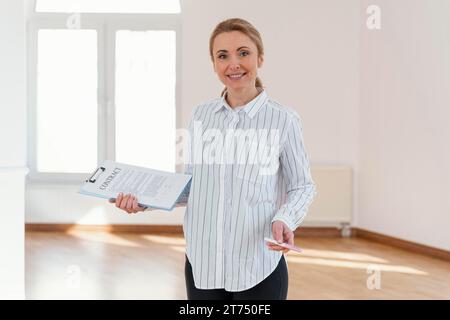 Vue de face smiley femme immobilier vide maison tenant le presse-papiers Banque D'Images