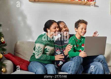 Joyeuse famille afro-américaine moderne assise sur un canapé ensemble regardant un film de Noël sur un ordinateur portable Banque D'Images
